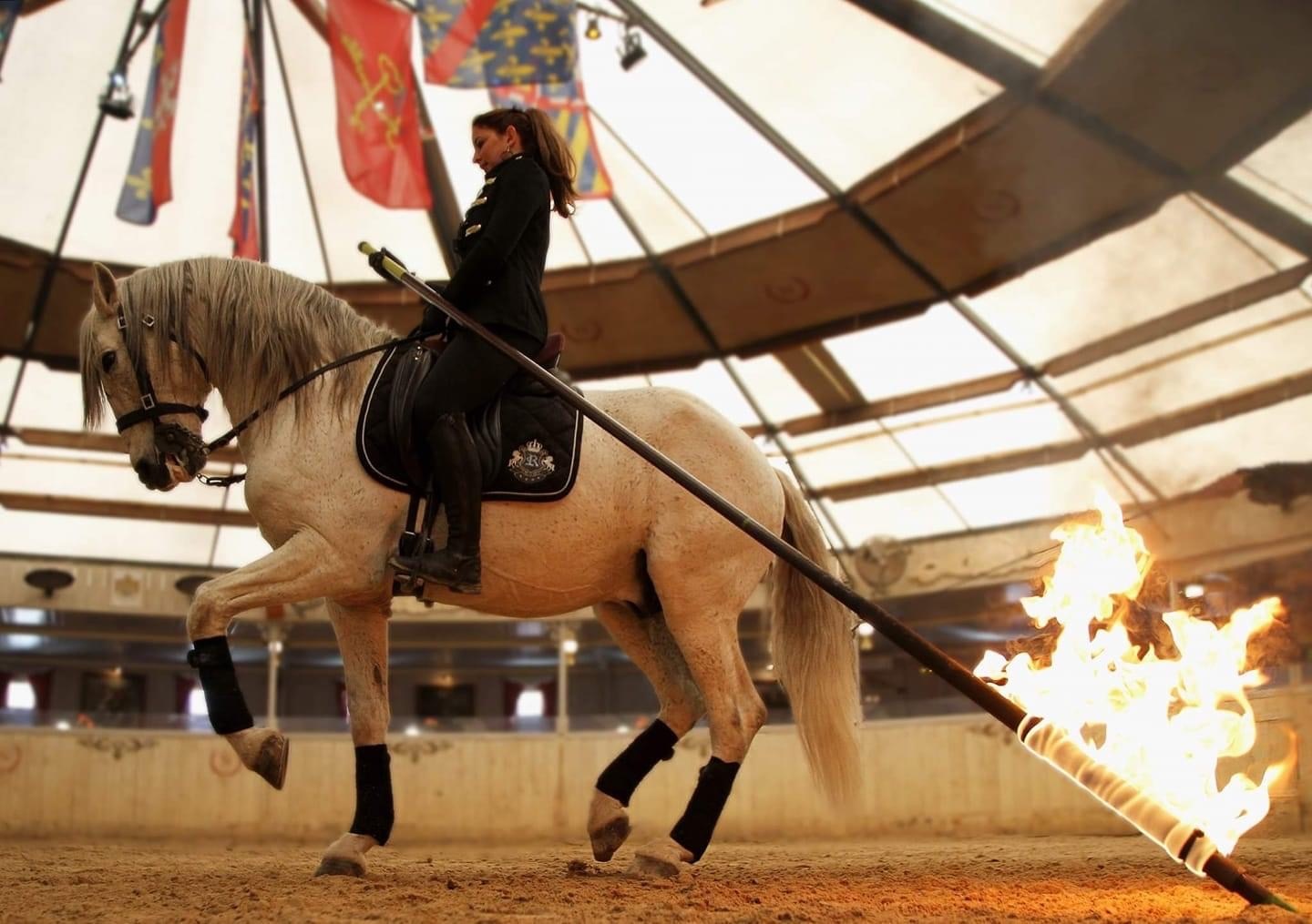 Cavalière sur un cheval clair pendant un numéro avec une torche dans le manège du Cabaret équestre des Mylords. Photo du partenaire.